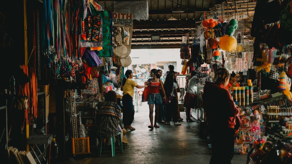 Vibrant indoor market scene with shoppers exploring diverse stalls filled with colorful merchandise.