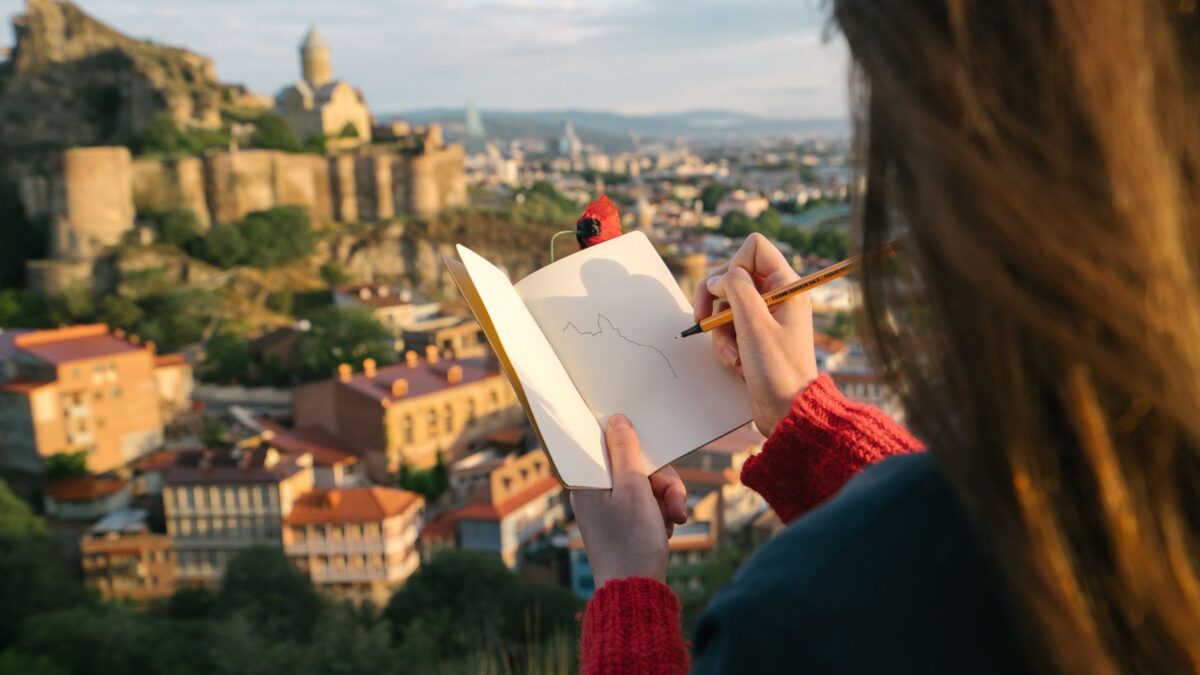 A person sketches a historic cityscape, capturing a picturesque scene with a castle at sunset.
