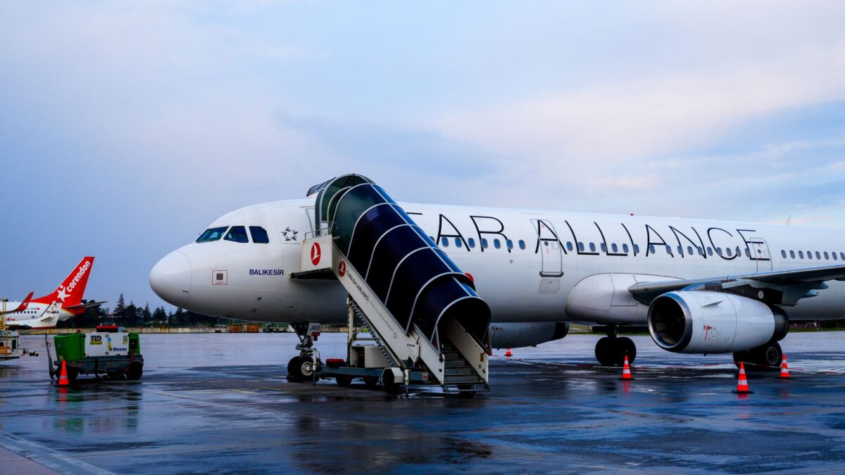 Commercial airplane on tarmac at İstanbul Airport with boarding stairs and cloudy sky.