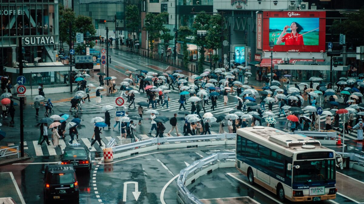 Crowds crossing Shibuya intersection in Tokyo under umbrellas on a rainy day.