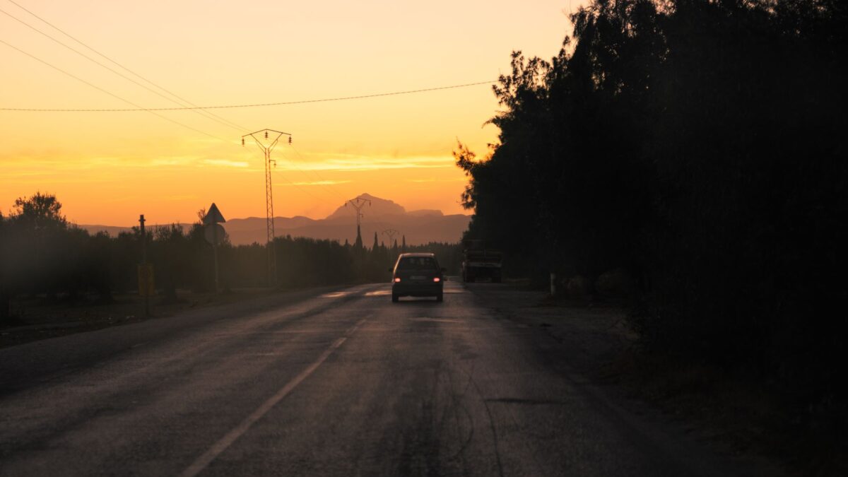 Car traveling on a scenic road at sunset near Tunis, captivating orange sky and silhouettes.