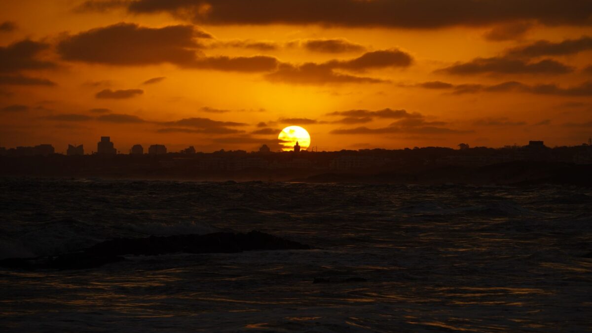 Silhouette of Punta del Este skyline with a dramatic sunset casting golden hues over the ocean.