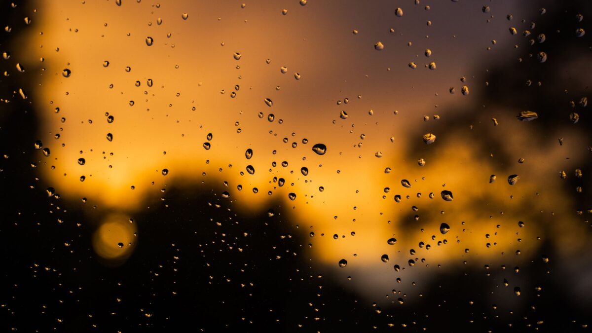 Raindrops on glass with a dramatic, vibrant sunset background.