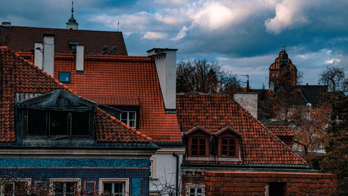 View of rustic rooftops in Warsaw's old town during autumn, framed by cloudy skies.