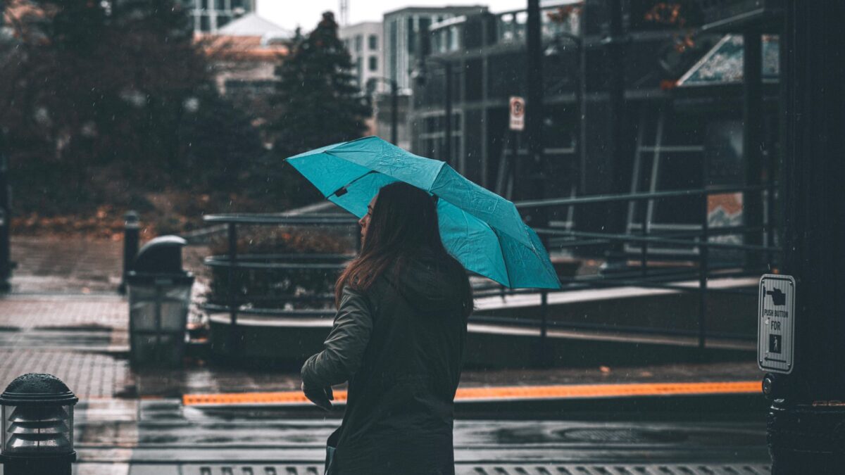 A woman with a blue umbrella walks through a city street on a rainy day, capturing the essence of urban life.