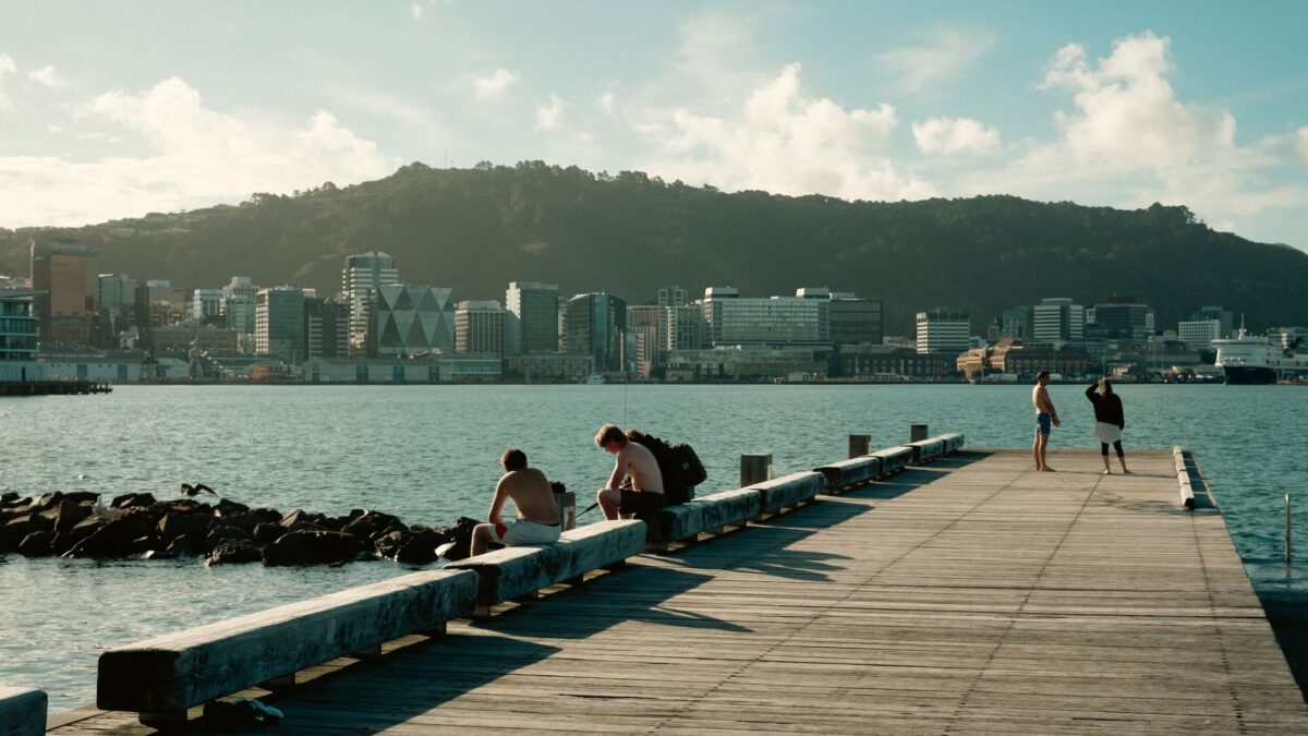 People enjoying a sunny day on the waterfront pier in Wellington, New Zealand with city skyline view.